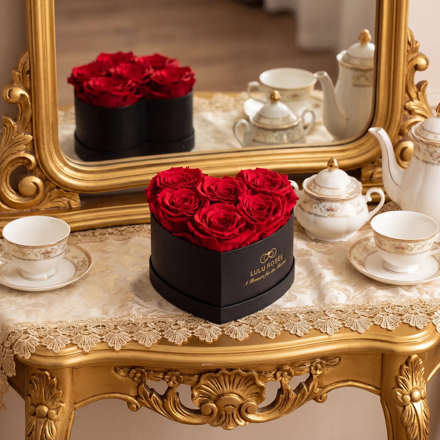 LULU ROSÉE baby heart box red roses black classic box displayed on  on a decorative table with teacups and a mirror in the background